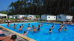 Een zwembad met mensen in het water, omringd door kleine hutjes en een bebost gebied.