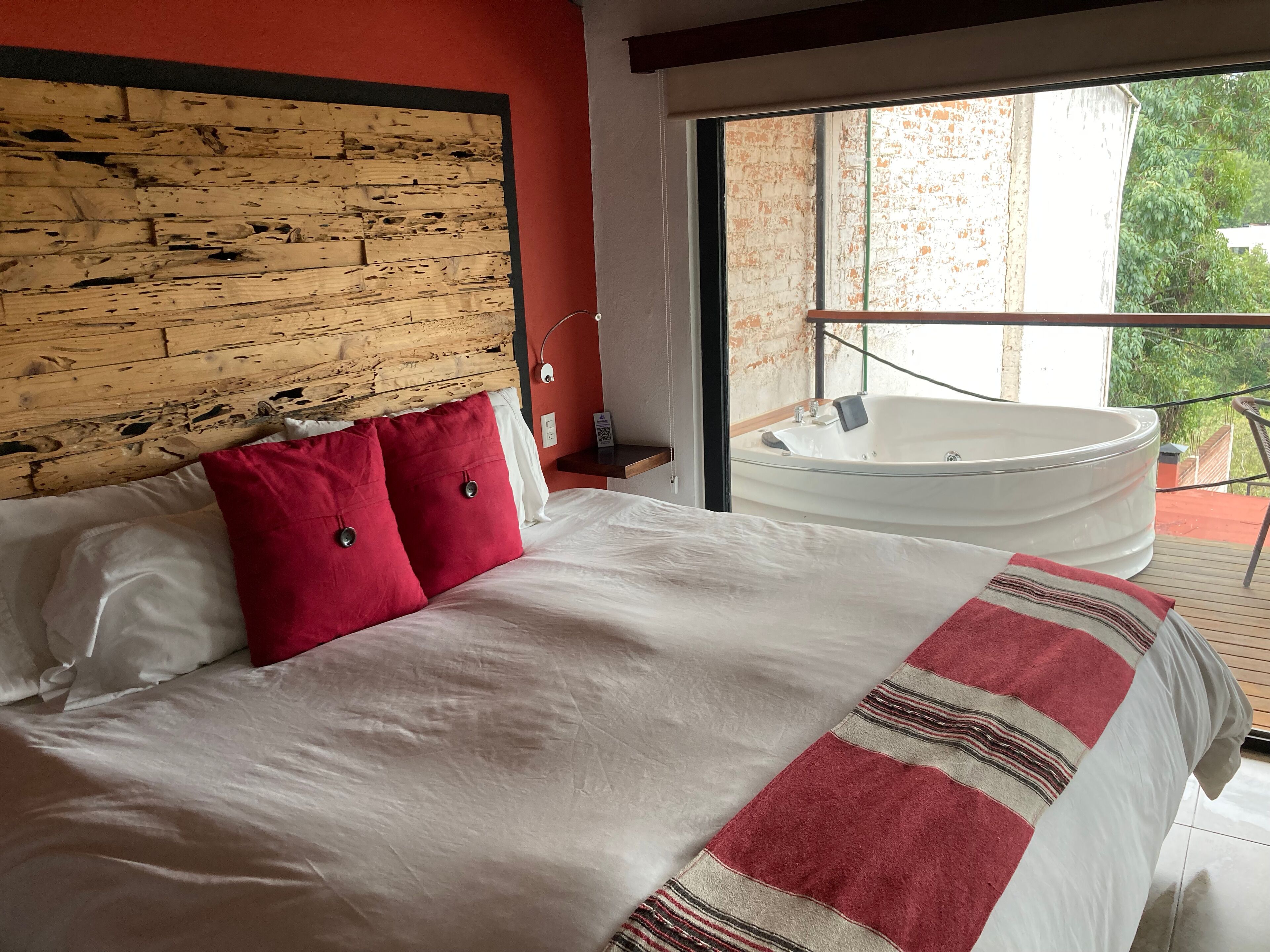 Hotellihuone, jossa on suuri sänky, puinen pääty, punavalkoraidallinen peitto ja lasiovesta näkyvä valkoinen kylpyamme.