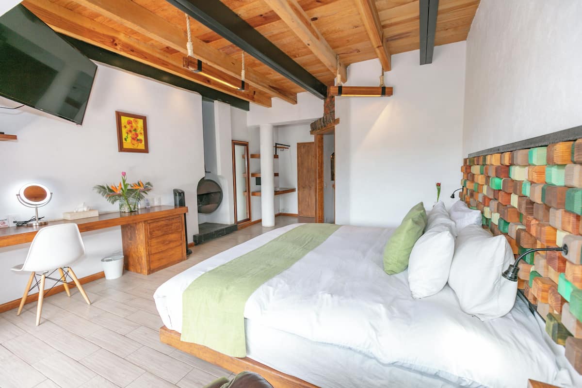 Un dormitorio con una cama grande, cabecera de madera, un escritorio con una silla, un televisor montado en la pared y un espejo.