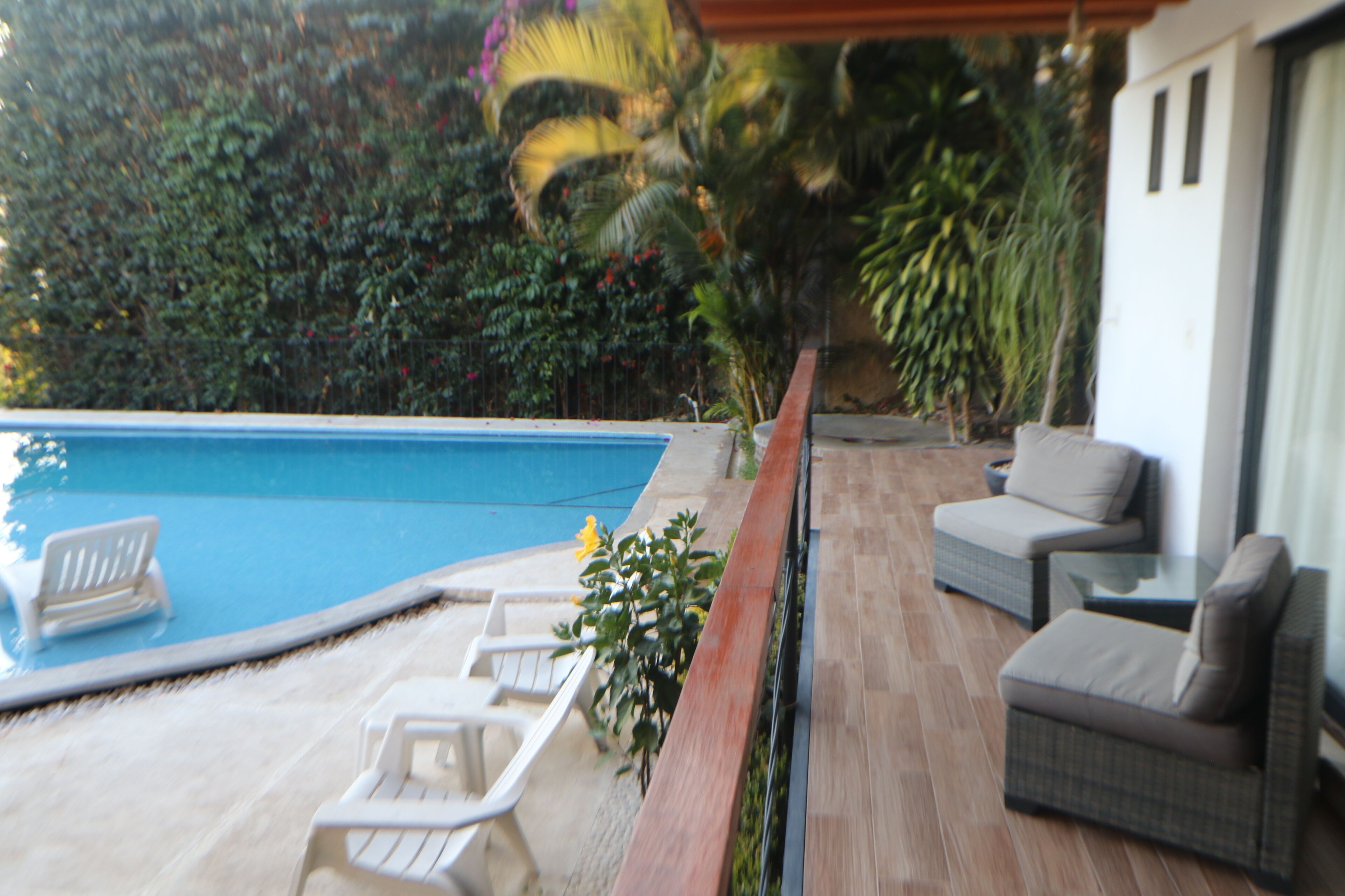 A pool area with lounge chairs and a wicker sofa.