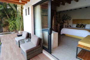 A room with a bed, a glass door leading to an outdoor area with a sofa and a table, and a potted plant.