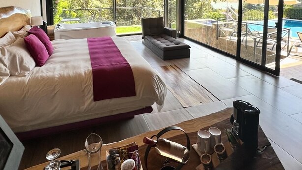 Un dormitorio amplio con una cama grande, vista a una piscina y techo de madera.