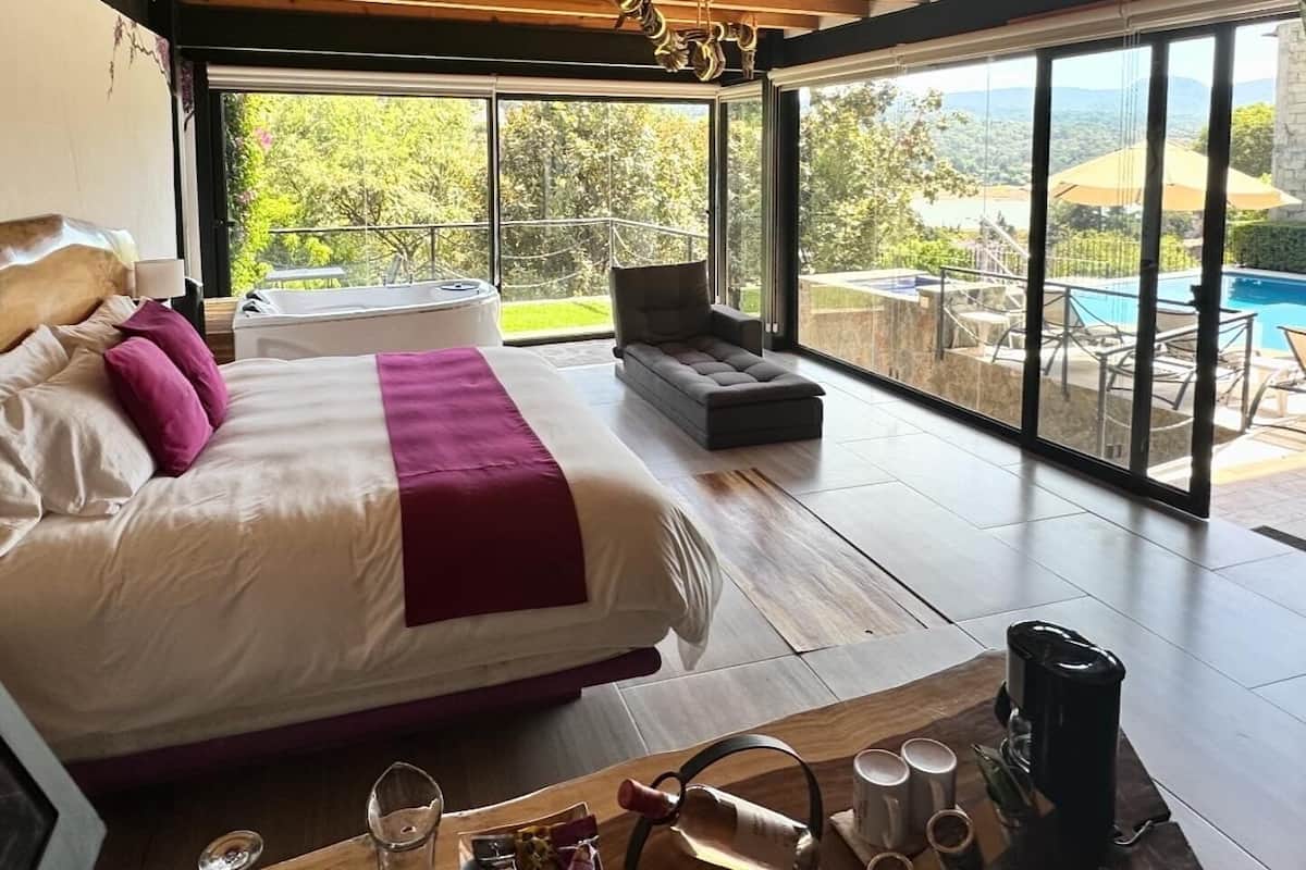 Un dormitorio amplio con una cama grande, vista a una piscina y techo de madera.
