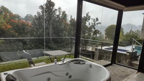 Un baño moderno con una bañera grande, zona de ducha con mampara de cristal y vistas a una piscina y montañas.