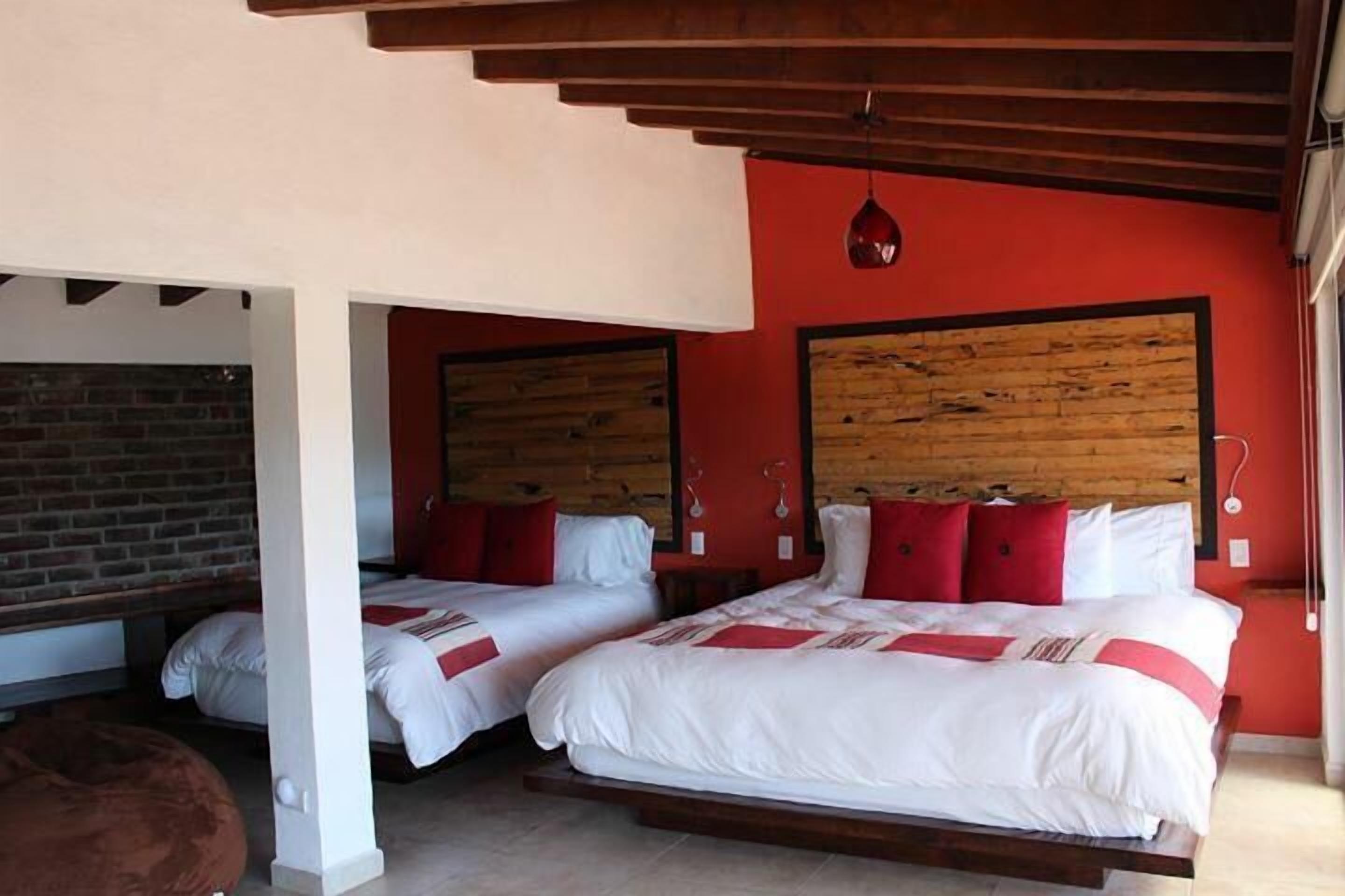 A room with two beds, red walls, wooden headboards, and a brick wall in the background.