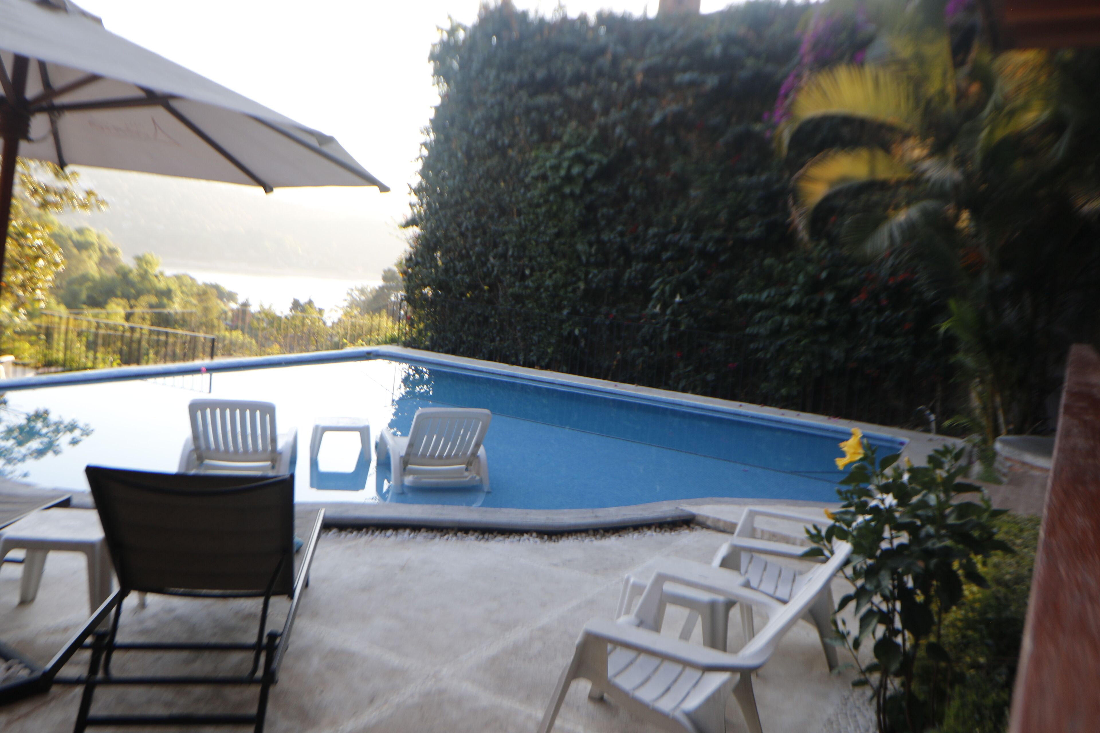 A swimming pool with white lounge chairs and an umbrella.