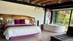 Un dormitorio con cama, sofá, bañera y vistas a la vegetación.
