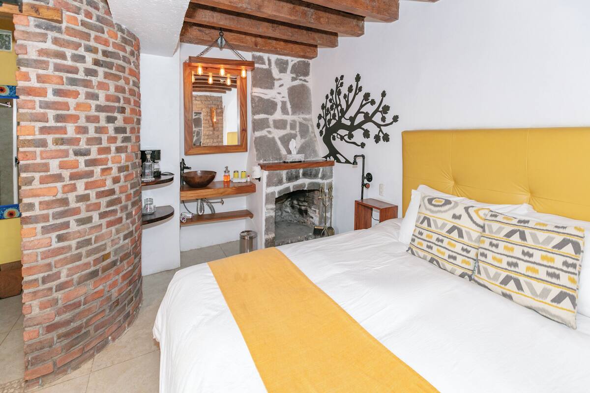 Un dormitorio con chimenea de ladrillo, una cama con cabecera amarilla y un adorno de árbol montado en la pared.