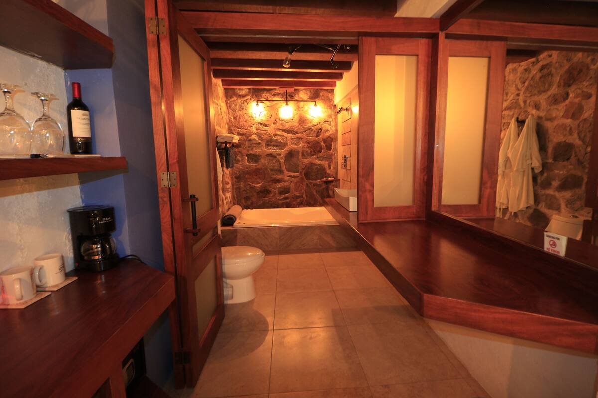 Un baño con pared de piedra, una bañera, un inodoro y un mostrador de madera con copas de vino y una cafetera.