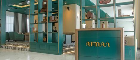 A modern hotel lobby with teal-colored walls, a marble floor, and a reception desk with 'AUTMAN' branding.