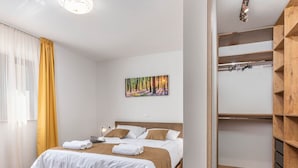 Un letto rifatto con lenzuola bianche e marroni, un laptop sul comodino e un quadro che raffigura una foresta al muro.