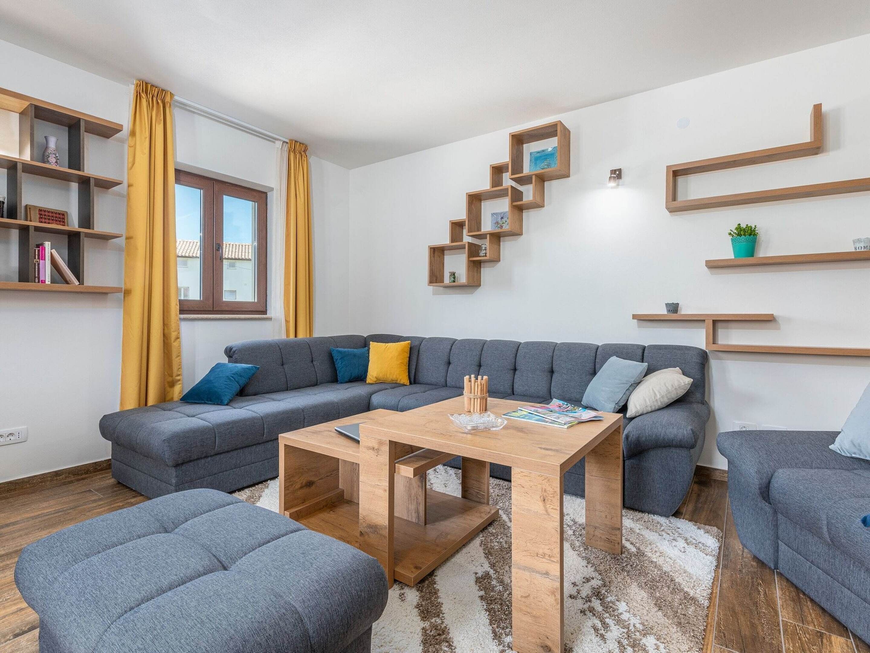 Una sala moderna con un sofá seccional gris, una mesa de centro de madera y estanterías empotradas de madera.
