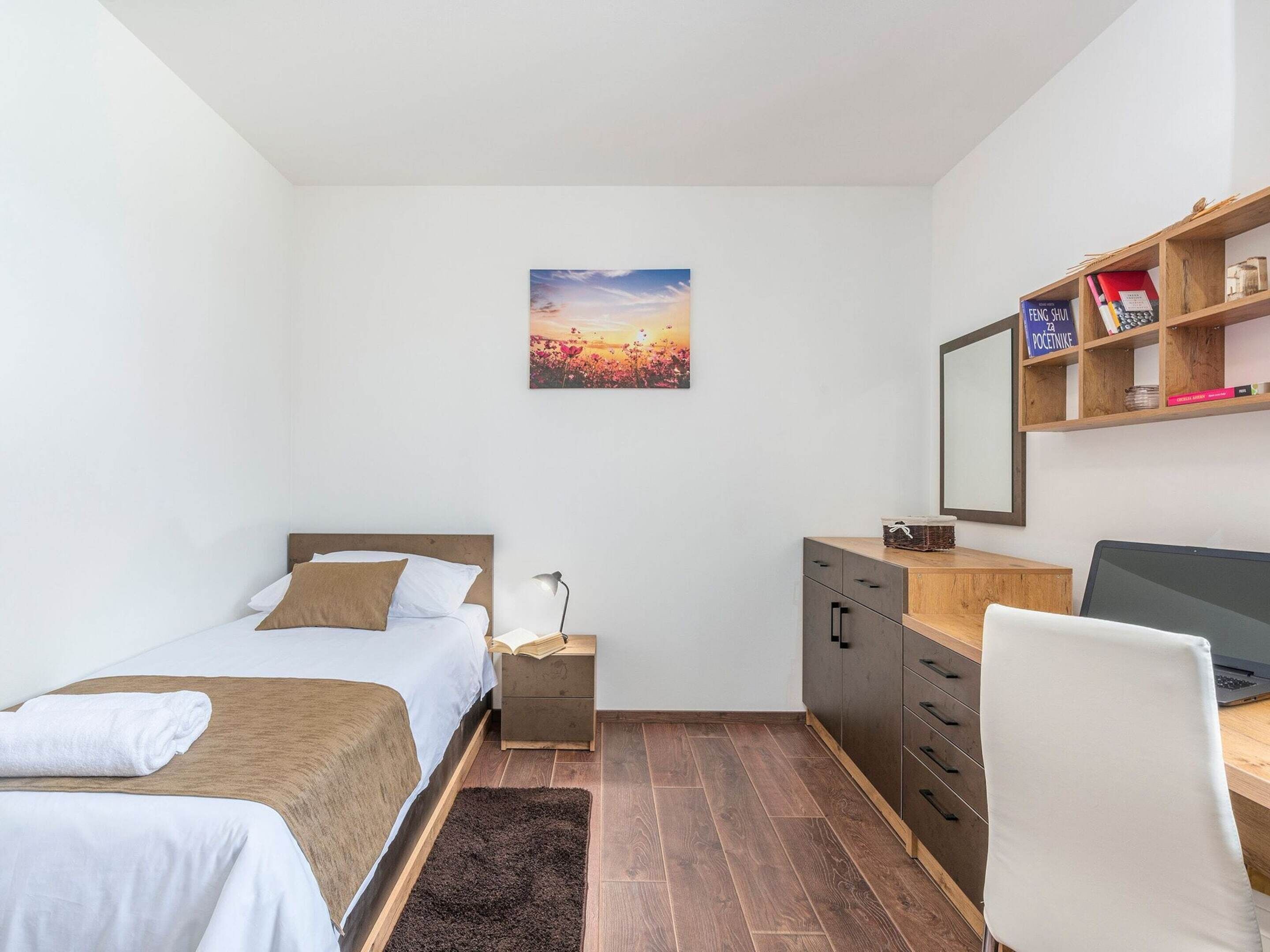 A compact bedroom with a bed, bedside table, desk, chair, and a bookshelf.