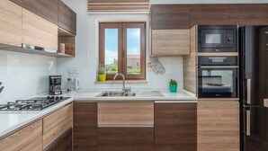 Una cucina moderna con mobili in legno, un lavello in acciaio inox, un piano cottura a gas, un forno a microonde e un forno integrato.