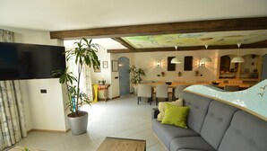 A living room with a sofa, coffee table, and a television. There is a dining area with chairs and a table, and a large potted plant. - Holiday Home in Haaren Near De Efteling (Haaren)