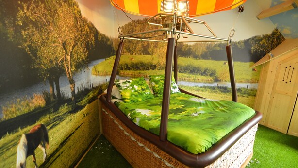 A cozy room with a wicker four-poster bed, a mural of a landscape, and a small wooden cabinet. - Holiday Home in Haaren Near De Efteling (Haaren)