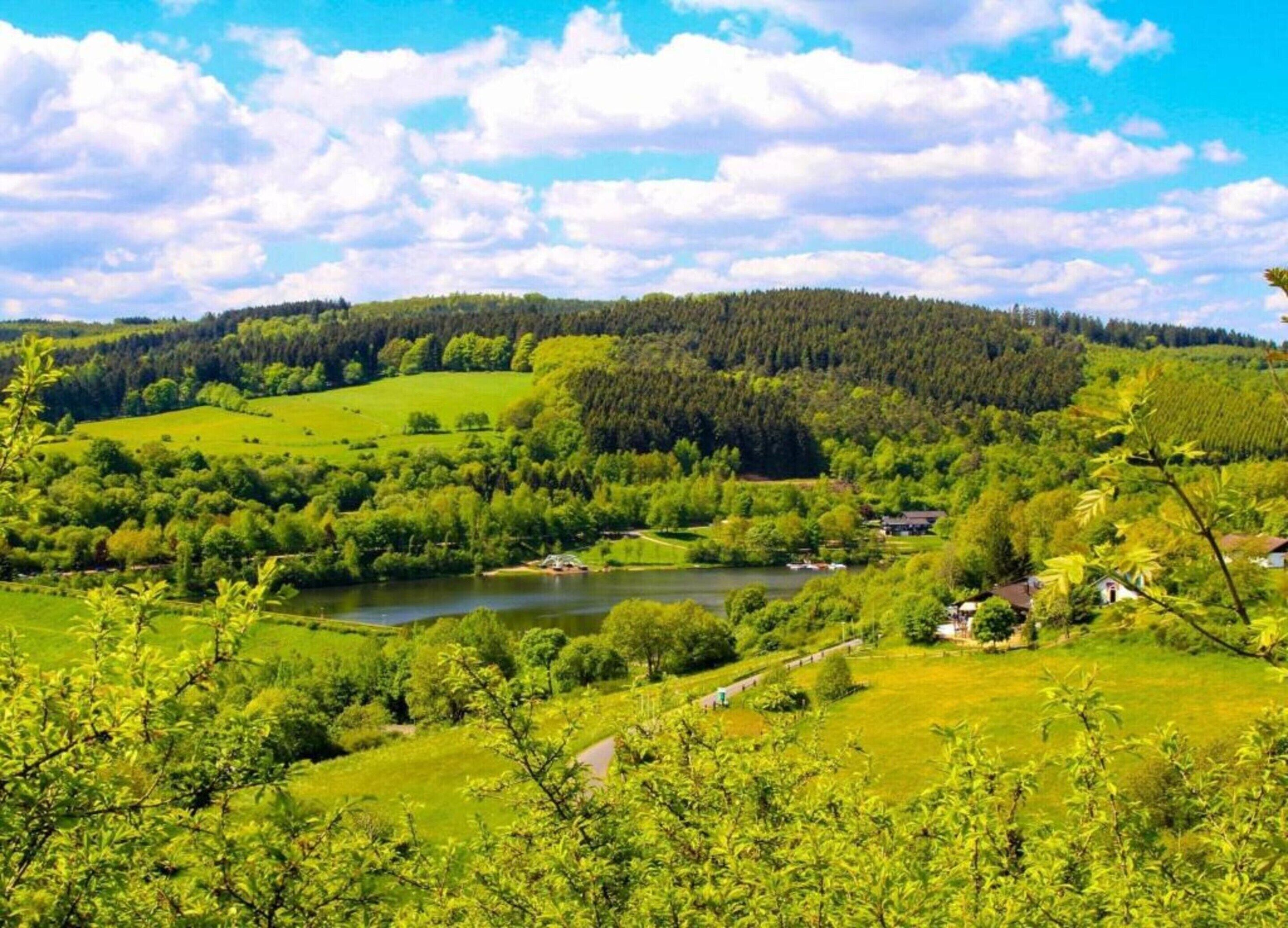 Uma paisagem verdejante com um rio, colinas e uma pequena casa.