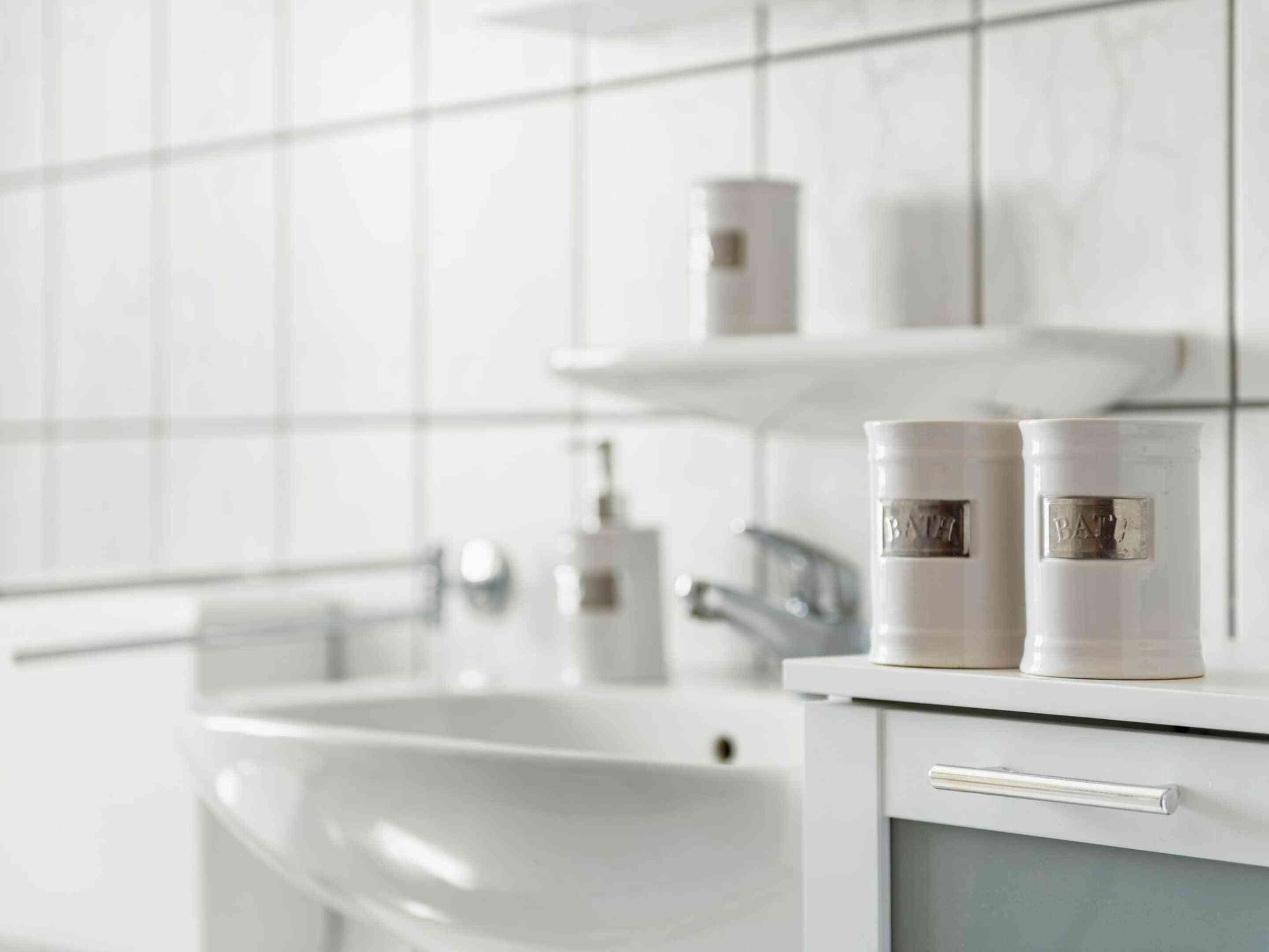 A bathroom with a white sink, mirror, and two white containers labeled "BAT" on a countertop.