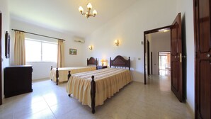 Ein Schlafzimmer mit zwei Betten, einer Chandelüster, einem Fenster mit Vorhängen und einer Tür zu einem anderen Raum.