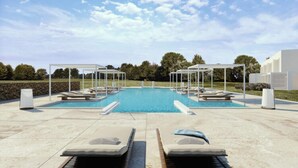 A swimming pool with lounge chairs and umbrellas, surrounded by a paved area and trees.