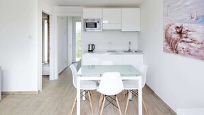 A modern kitchen with white cabinets, a microwave, and a sink. There is a glass dining table with white chairs.