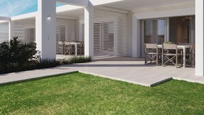 A modern outdoor patio area with white walls and slatted roof design, featuring multiple seating arrangements and a well-maintained lawn.