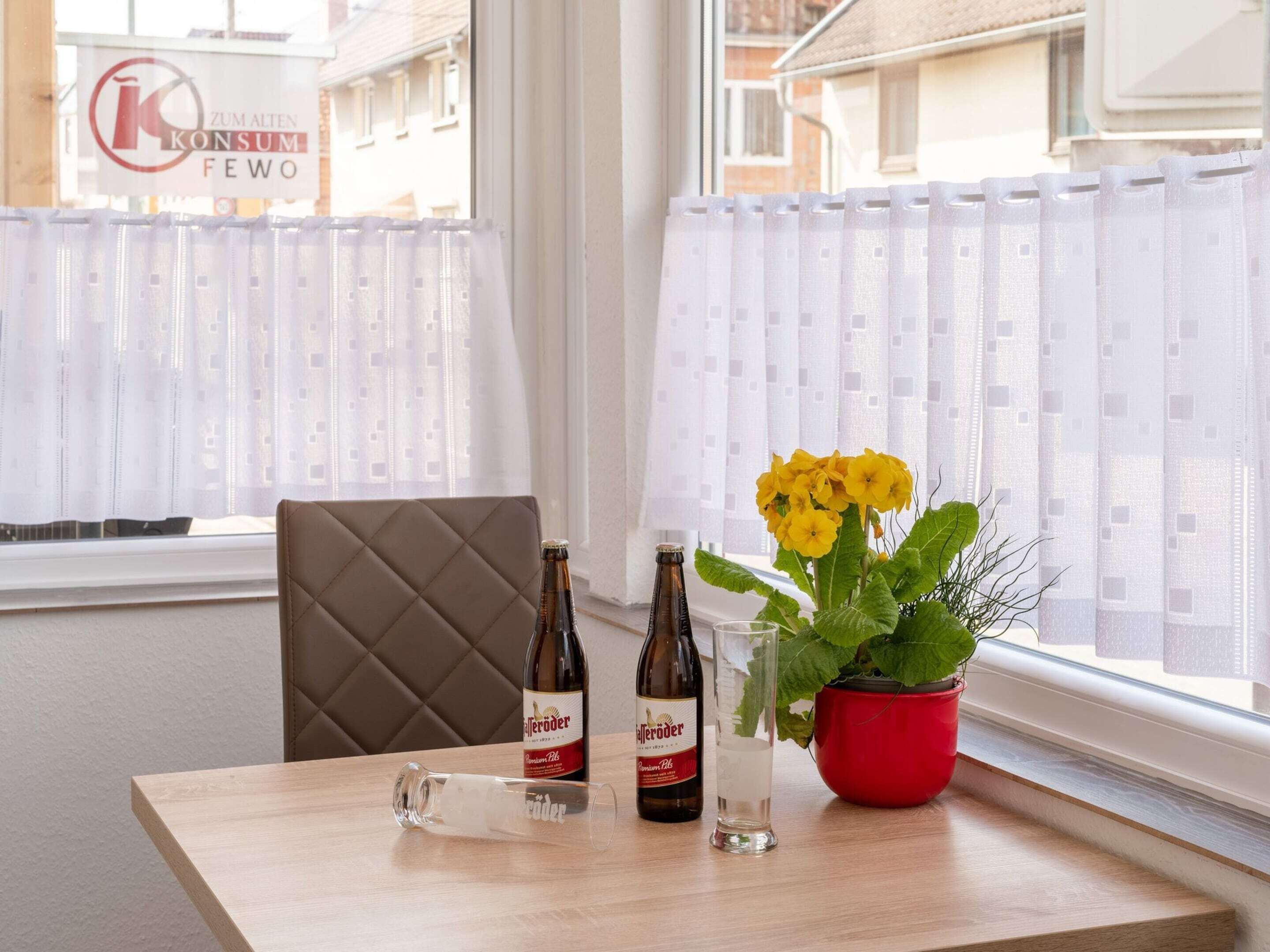 A table with two bottles of beer, a glass, and a potted plant with yellow flowers.