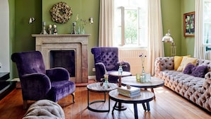 A cozy living room with a fireplace, green walls, and a large window with curtains. There are two purple armchairs, a tufted sofa, and a round coffee table. - Sprawling Farmhouse in Baarlo With Hot Tub, Private Garden (Baarlo)