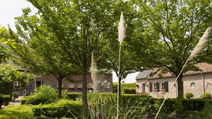 Un giardino con uno stagno, vegetazione lussureggiante e un edificio in mattoni con tetto in tegole.
