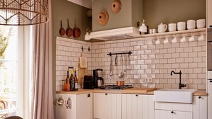 Cucina con mobili bianchi, un piano di lavoro in legno, un fornello a gas e un lavandino. Si notano pentole e padelle appese, una macchina da caffè e un portabottiglie.