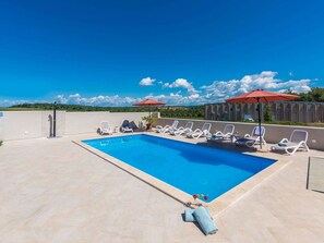A swimming pool with lounge chairs and umbrellas, surrounded by a low wall and a clear sky. - Villa in Novigrad With Private Pool (Novigrad)