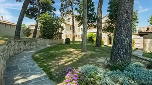 A stone pathway leading to a courtyard with a stone building, surrounded by trees and a small flower bed. - Serene Apartment With Pool (Mombaroccio)