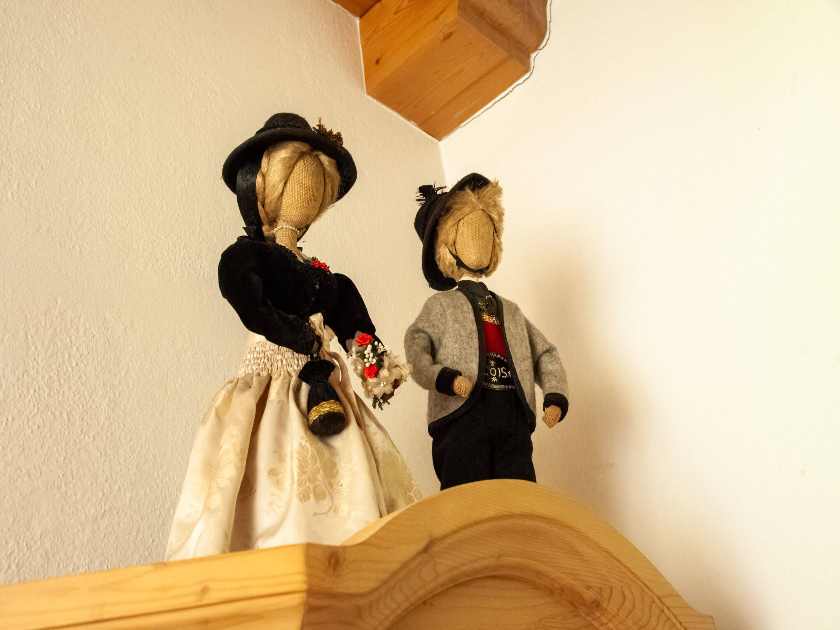 Two dolls dressed in period costumes on a wooden shelf against a plain wall.
