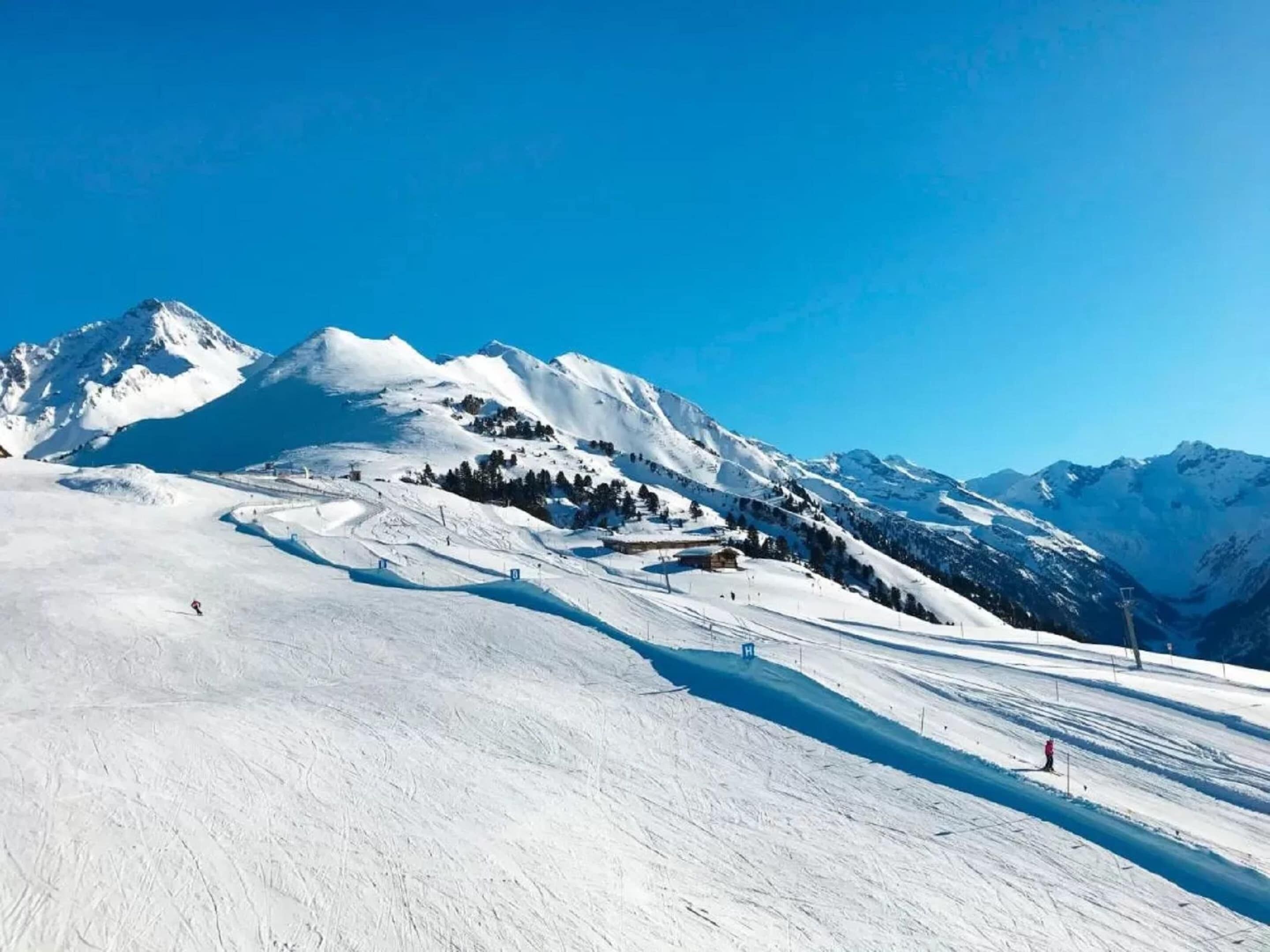 Un paysage de montagne enneigé, avec des pistes de ski et un ciel bleu dégagé.