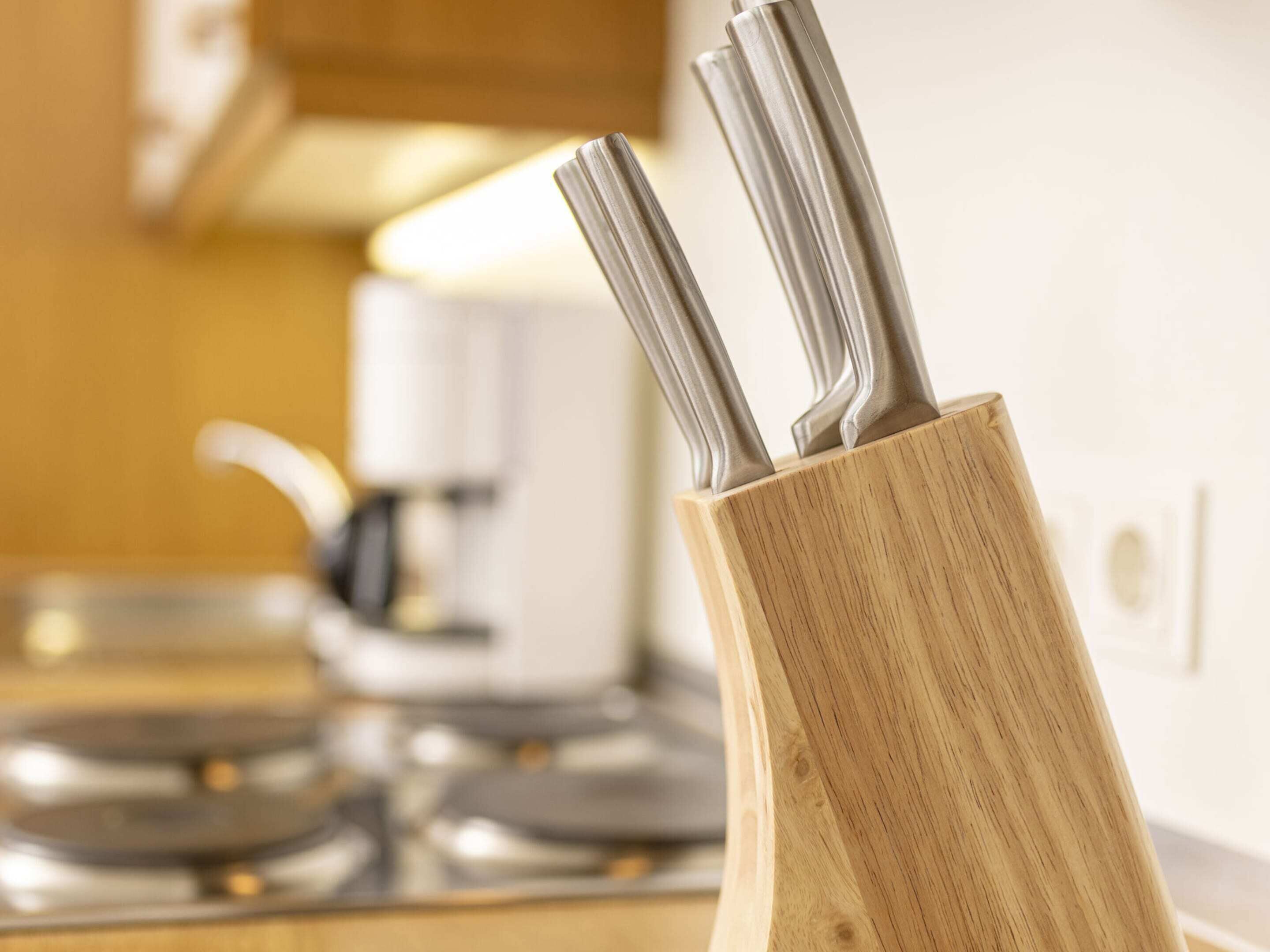 A wooden utensil holder with metal utensils on a kitchen counter.