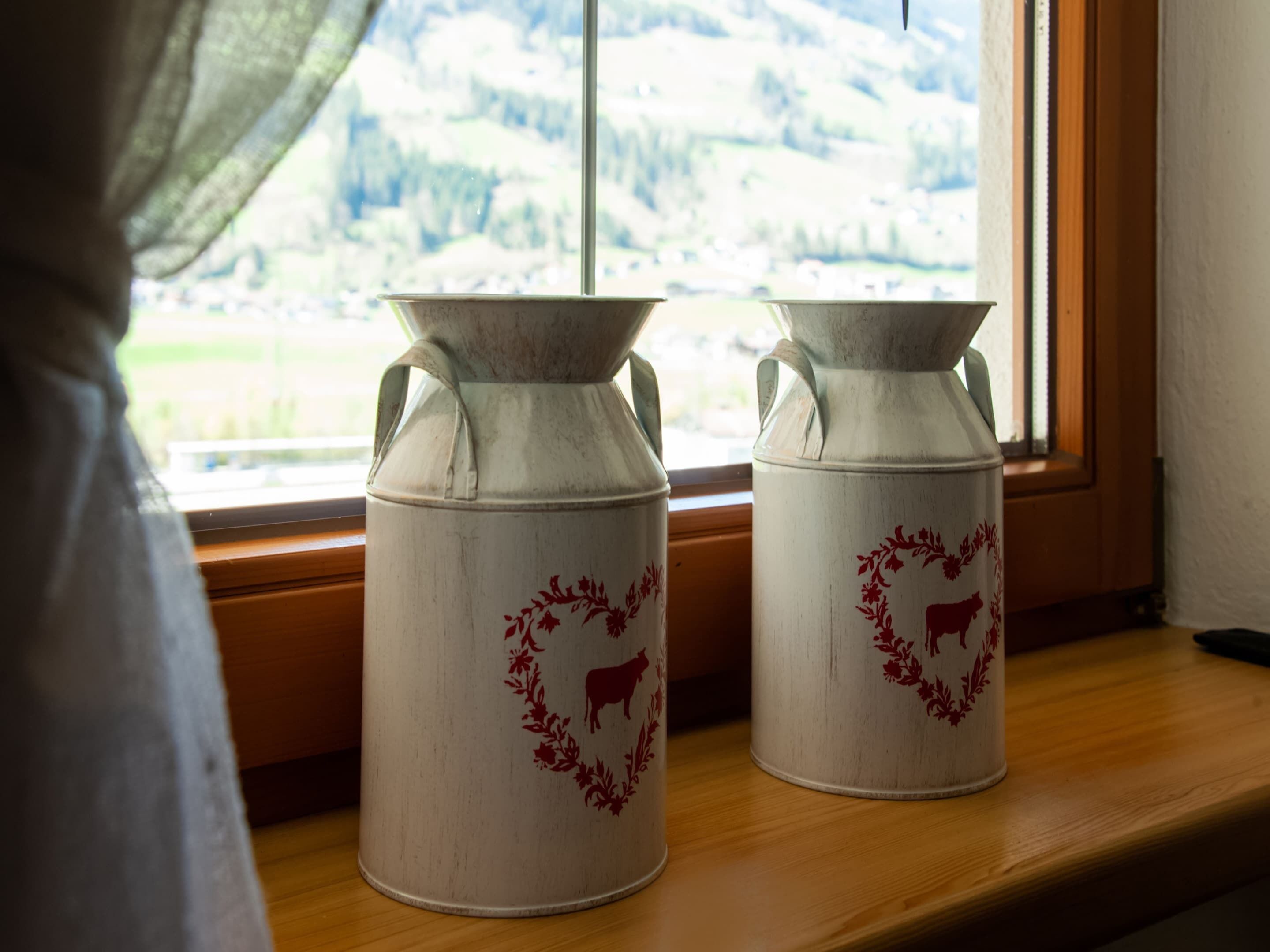 Dues gerres de ceràmica blanca amb motius florals i d'animals sobre una prestatgeria de fusta al costat d'una finestra.