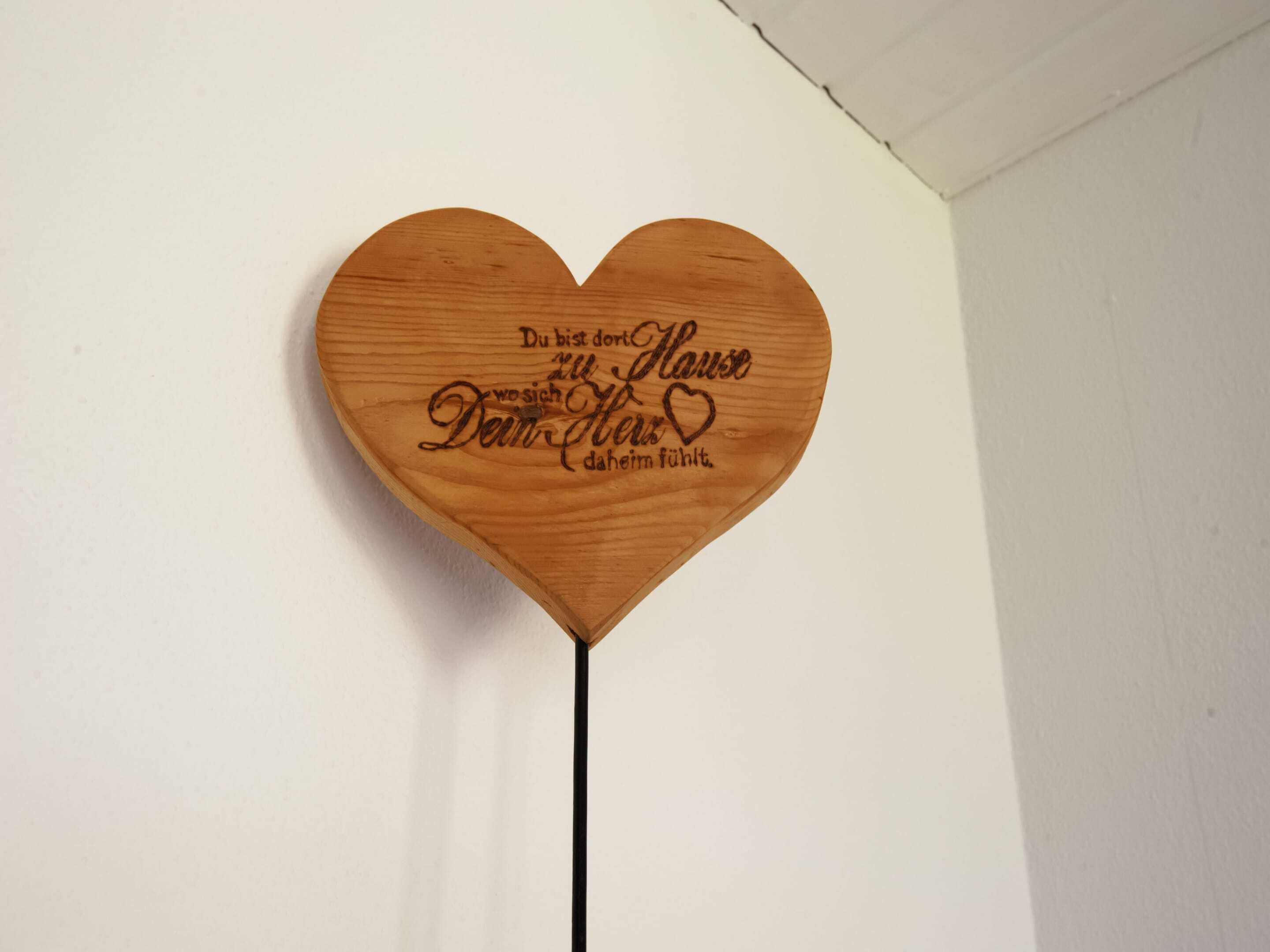 Een houten hartvormig bord met tekst in het Duits, bevestigd aan een muur.