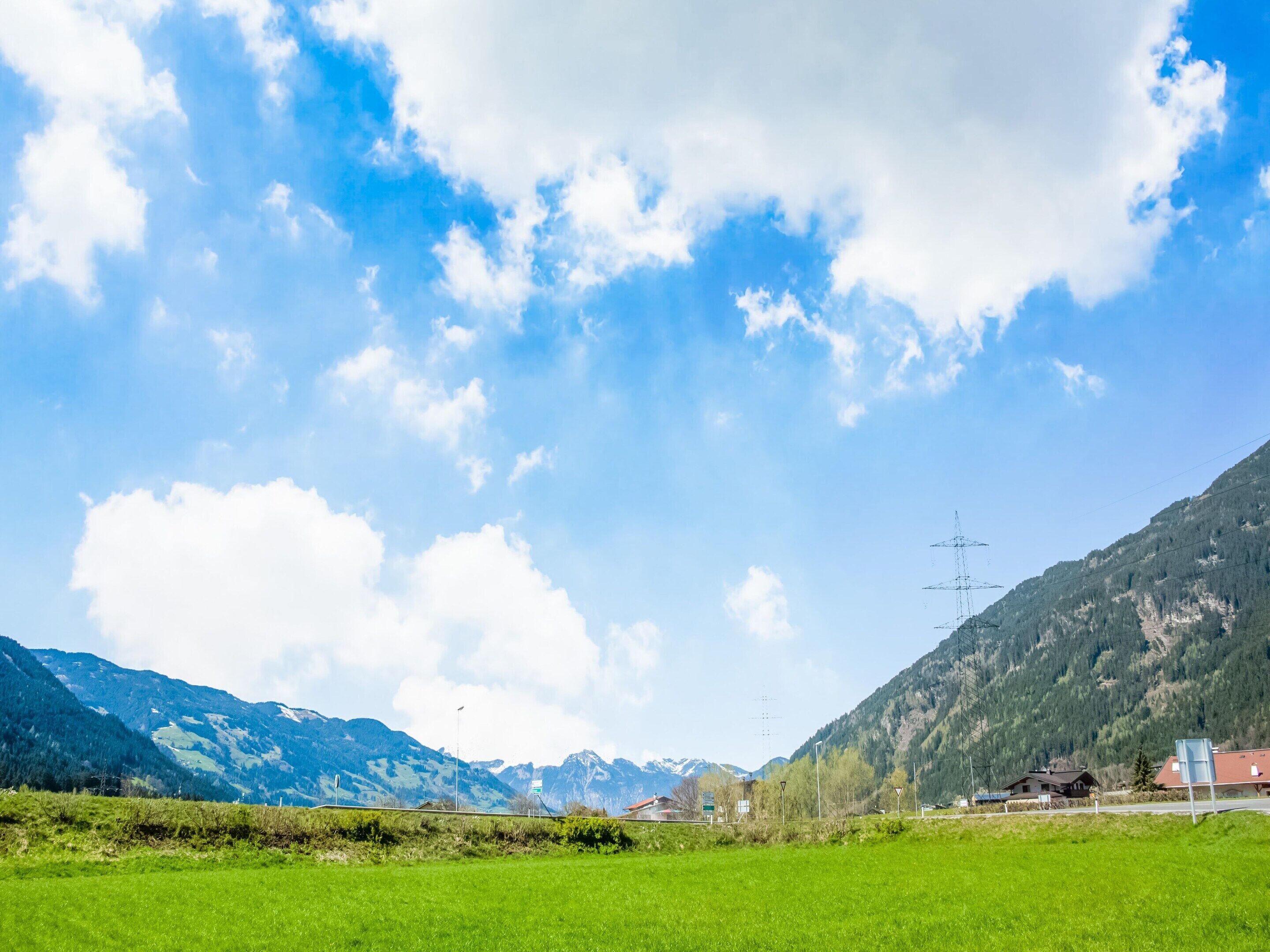 Paisaje rural con cielo despejado, campos verdes y montañas al fondo.