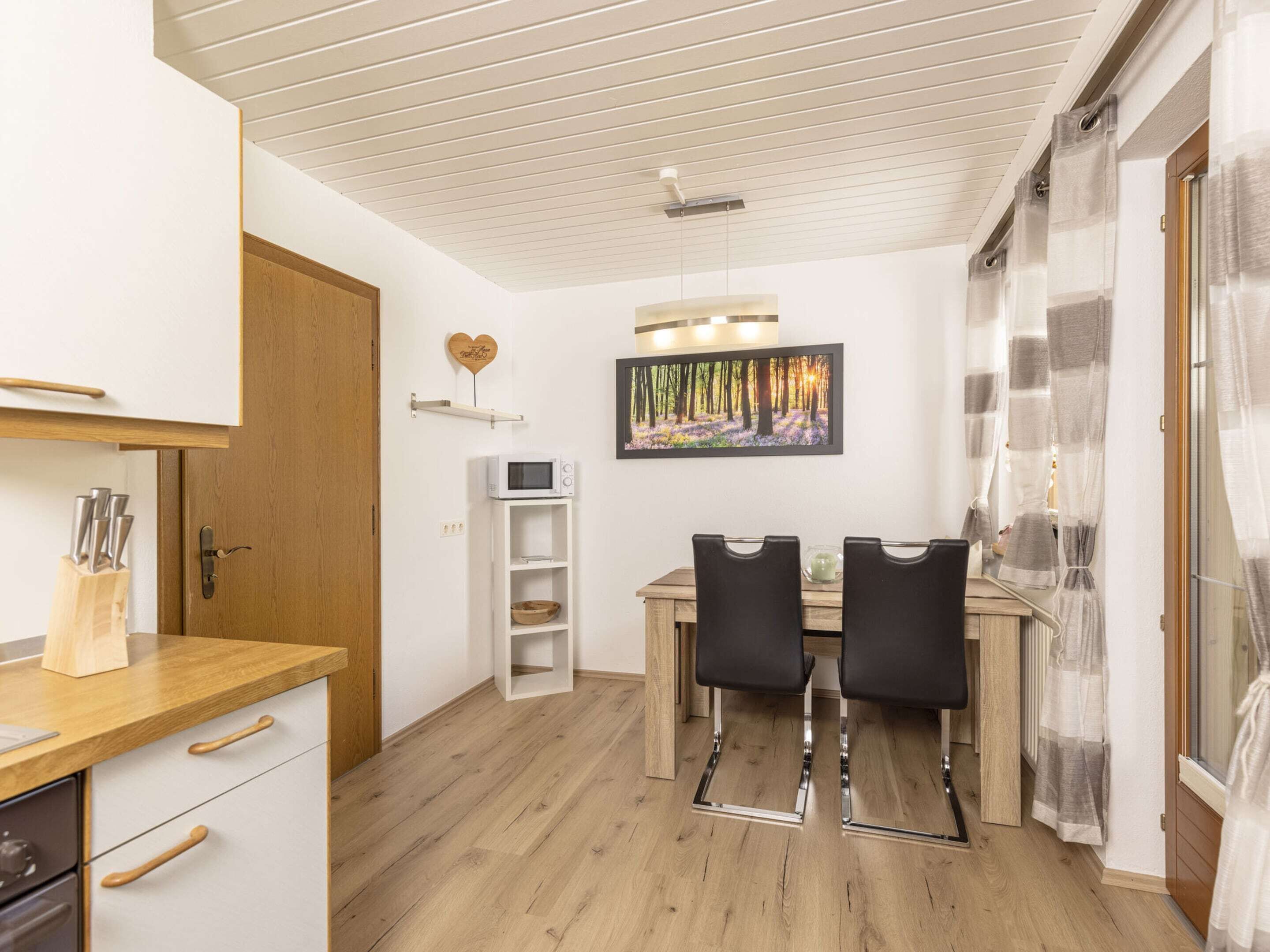A modern kitchen with wooden cabinets, a white microwave, and a dining area with two black chairs and a wooden table.