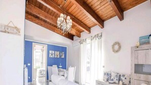 Une pièce avec un canapé blanc, un plafond en bois et un lustre. Un mur bleu est décoré d’œuvres d’art représentant des étoiles de mer, et une armoire blanche contient des objets décoratifs.