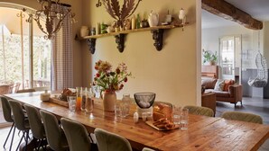 Comedor con mesa de madera, sillas, una lámpara de araña y estante con utensilios de cocina.