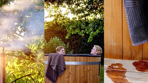 Una bañera de hidromasaje de madera con estructura metálica, rodeada de follaje.