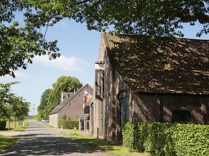 A brick building with a tiled roof, a flag, and a hedge in front. - Beautiful Farmhouse in Baarlo With Private Garden (Baarlo)
