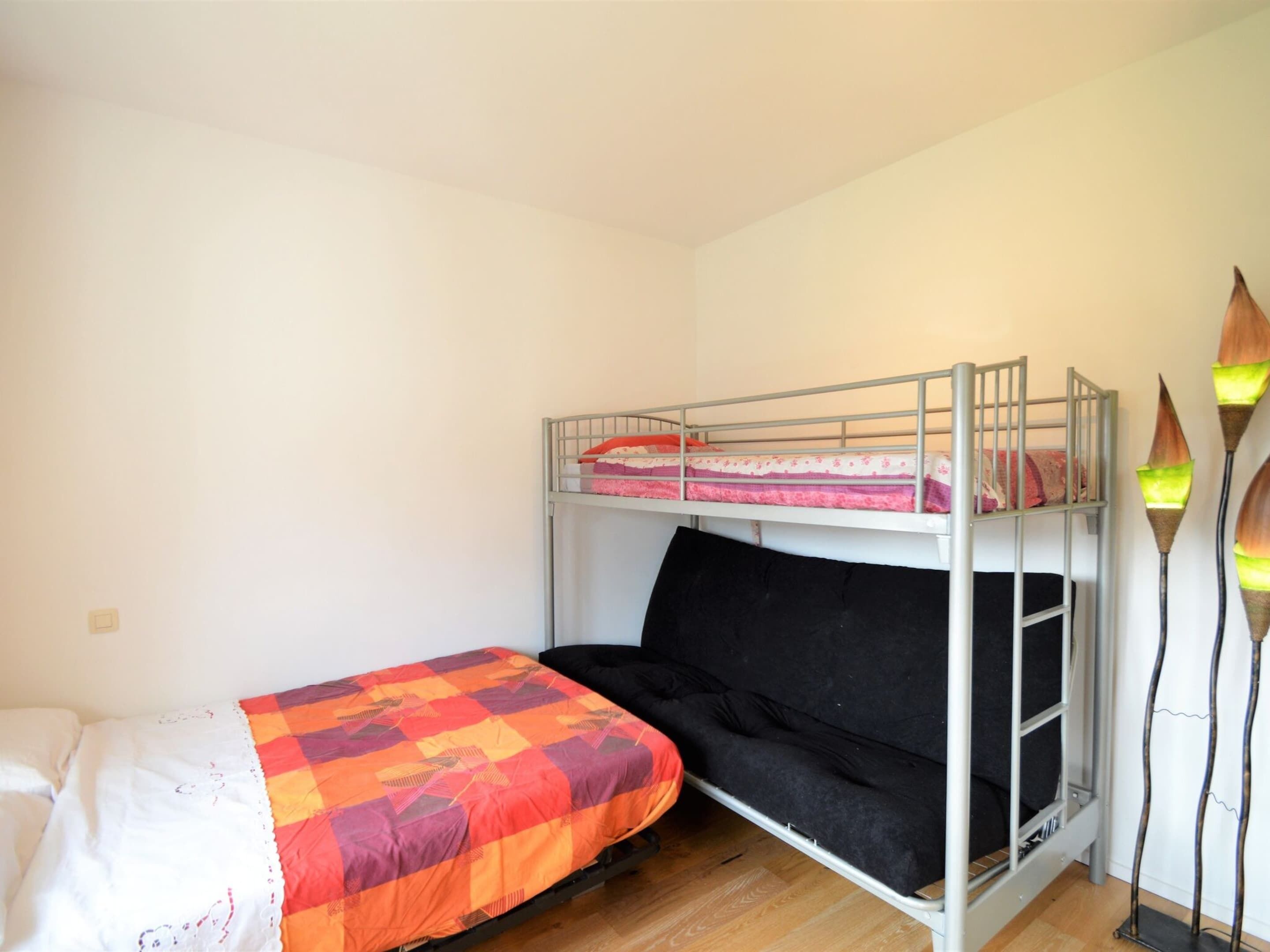 A dormitory room with a bunk bed, a single bed, and a decorative floor lamp.
