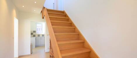 A wooden staircase leading to an upper floor, with a kitchen area visible in the background.