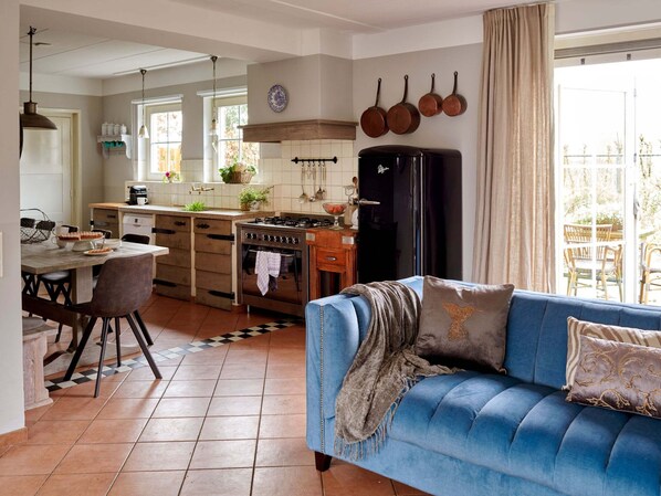 Een moderne keuken met een centraal eiland, een zithoek met een blauwe bank en uitzicht op de omgeving.