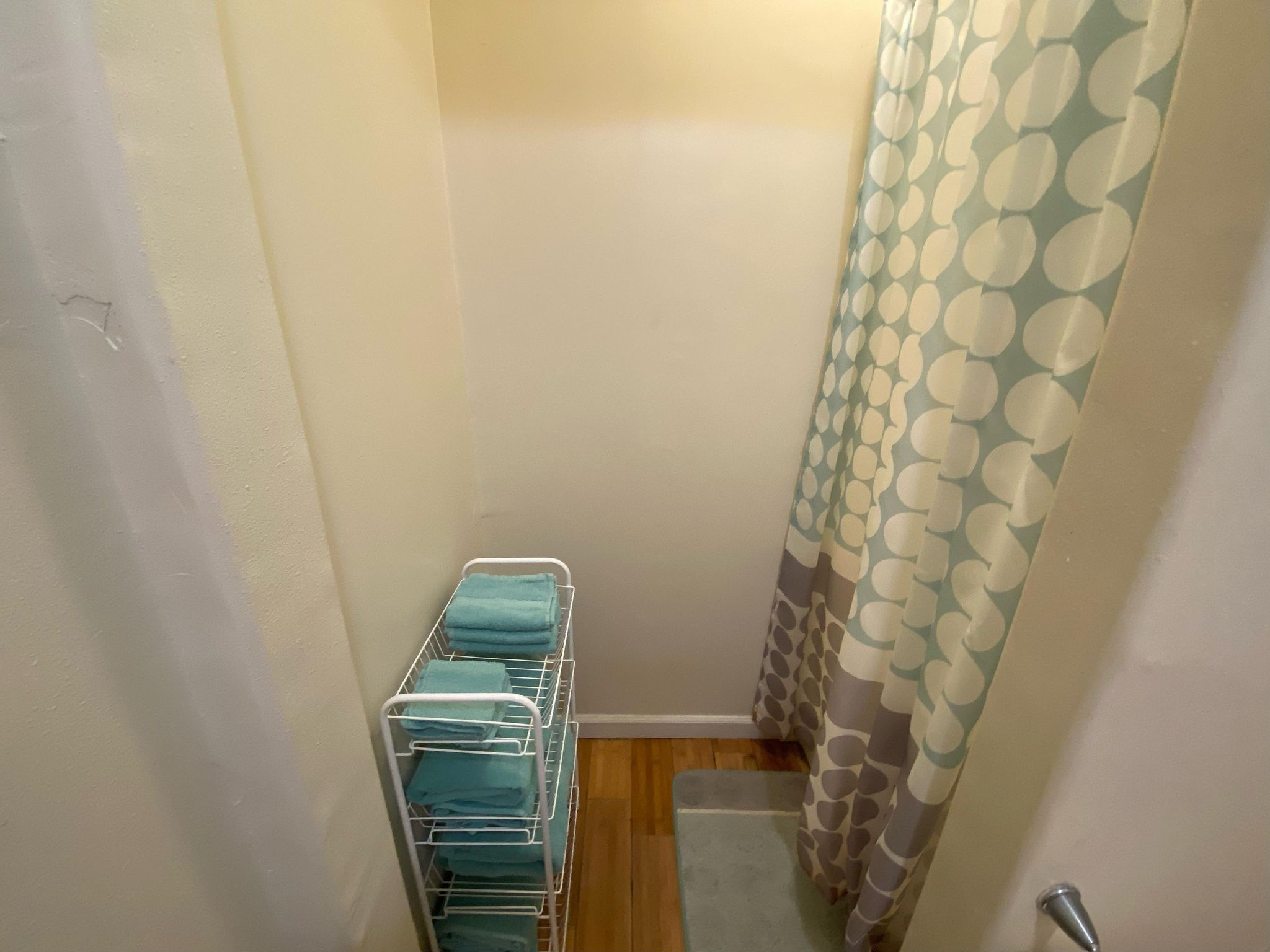 Une salle de bain avec un porte-serviettes blanc sur lequel sont pliées plusieurs serviettes. On aperçoit une partie d’un rideau de douche à motifs.