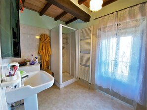 Ein Badezimmer mit Waschbecken, Spiegel, Dusche und einem Fenster mit Vorhang.