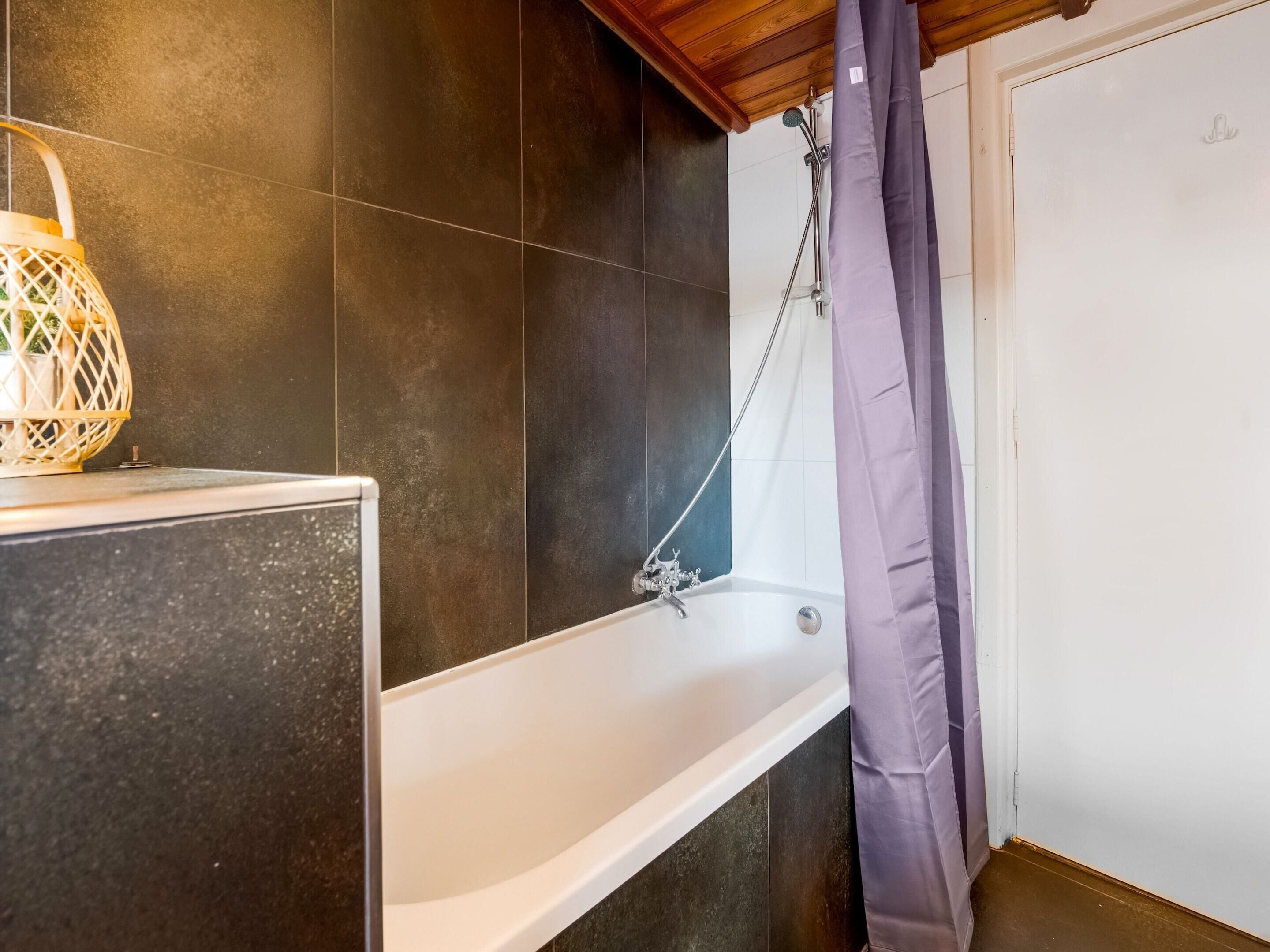 A bathroom with a bathtub, dark tiles, a wooden ceiling, and a shower curtain.
