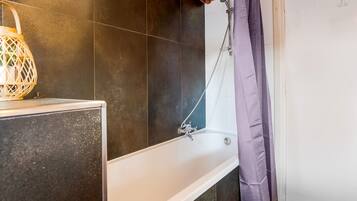 A bathroom with a bathtub, dark tiles, a wooden ceiling, and a shower curtain.
